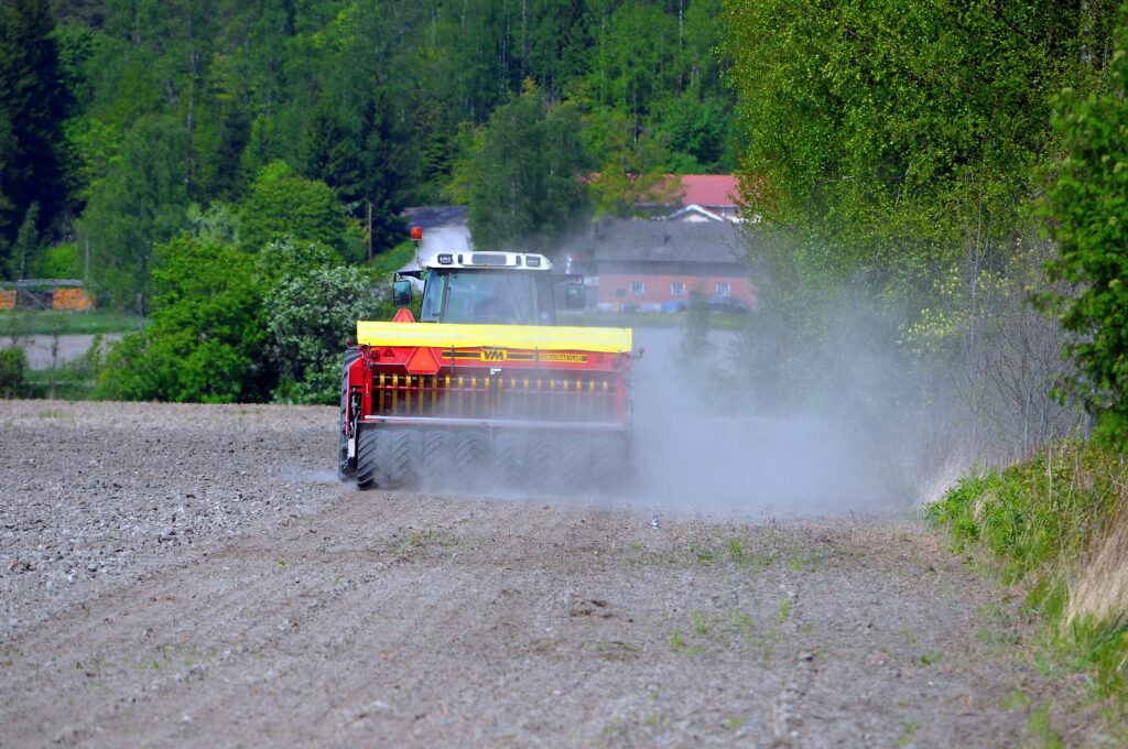 Traktor kör med såmaskin på en torr åker så att det dammar.