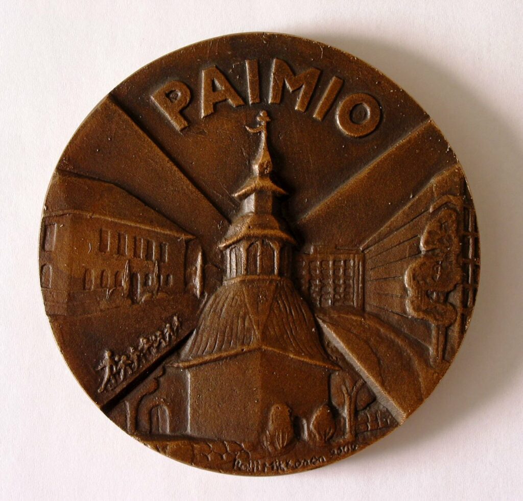 Pronssinen Paimio-mitali, jonka kuva-aiheina yhteiskoulun rakennus, kirkon kellotapuli ja Paimion parantola