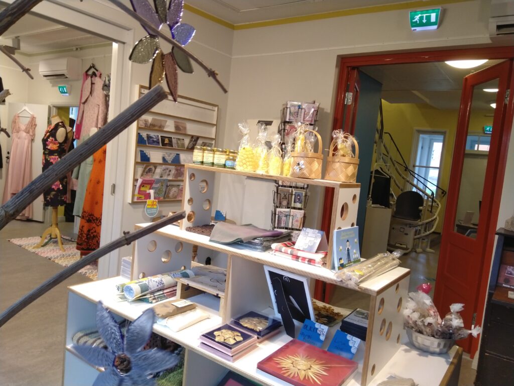 Museokauppa Käsityömuseo Miilassa. Etualalla myyntituotteita, taustalla näkyy porrasnostin, jolla voi liikkua näyttelykerrosten välillä.