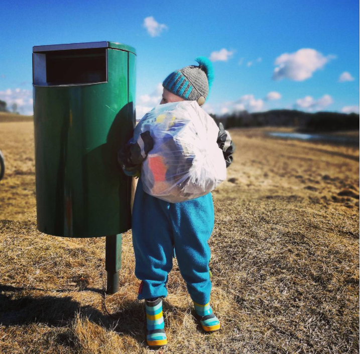 Roskiksen vieressä seisova lapsi on kerännyt ison pussillisen roskia.
