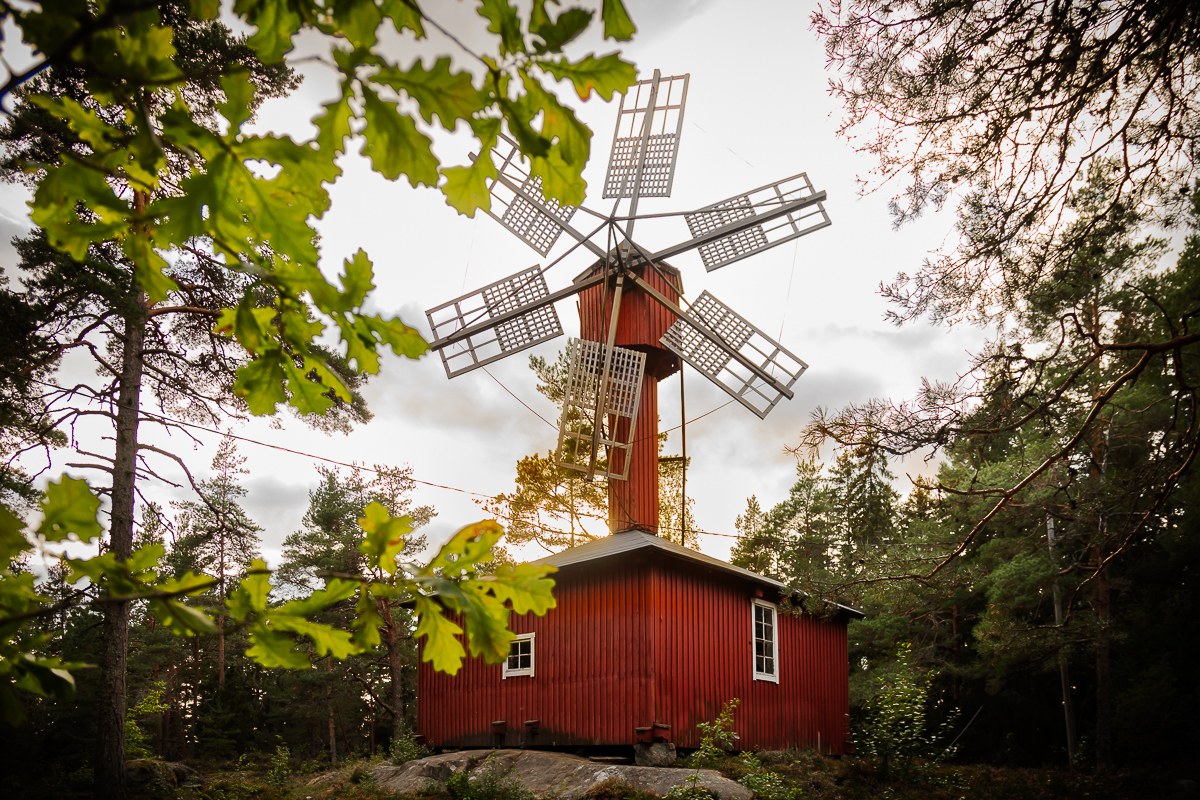 Punainen, puonen, tuulimylly, jonka ympärillä kasvaa puita.