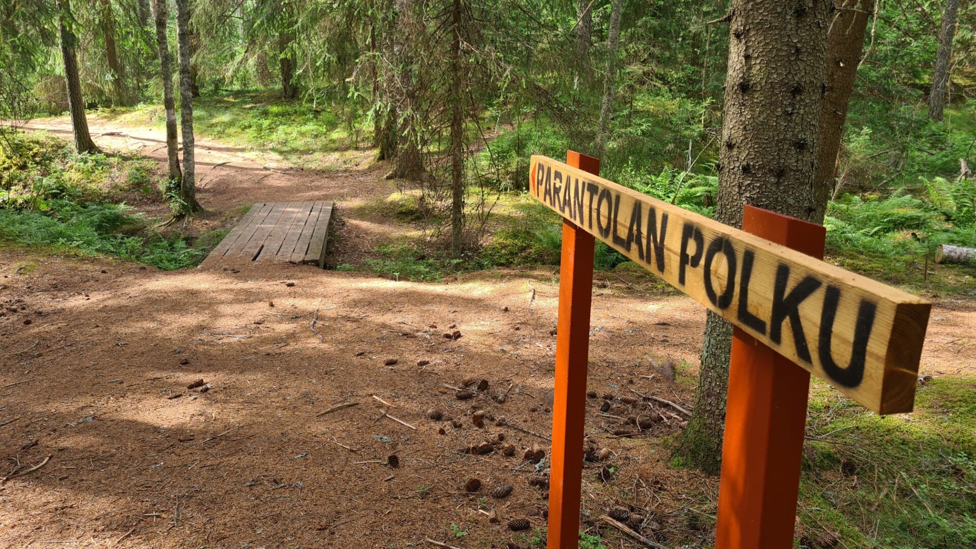 Polku kuusimetsässä. Etualalla puinen opasteviitta, jossa lukee Parantolan polku.