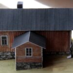 Pyölniitun museon pienoismalli, jossa 1,5 kerroksinen, kellertävä puurakennus. Pihamaalle on sijoitettu seisomaan yksi mieshenkilö.
