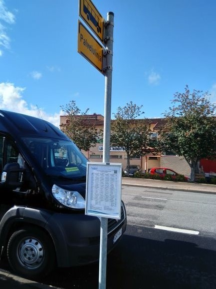 Palveluliikenteen auto pysäkillä, jossa myös palveluliikenteen aikataulukyltti.
