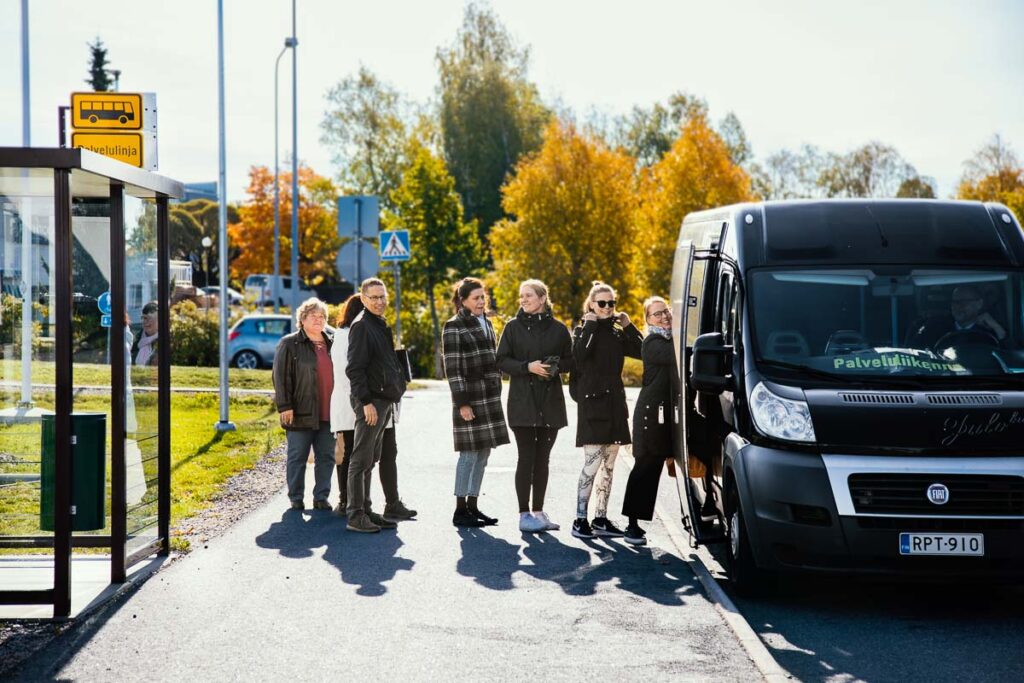 Ihmisiä nousemassa pysäkiltä palveluliikenteen bussin kyytiin.