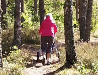 Nainen kävelyllä metsäpolulla maastorollaattorin avulla.