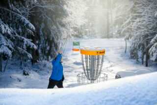 Frisbeegolfin heittäjä talvisessa metsämaisemassa.