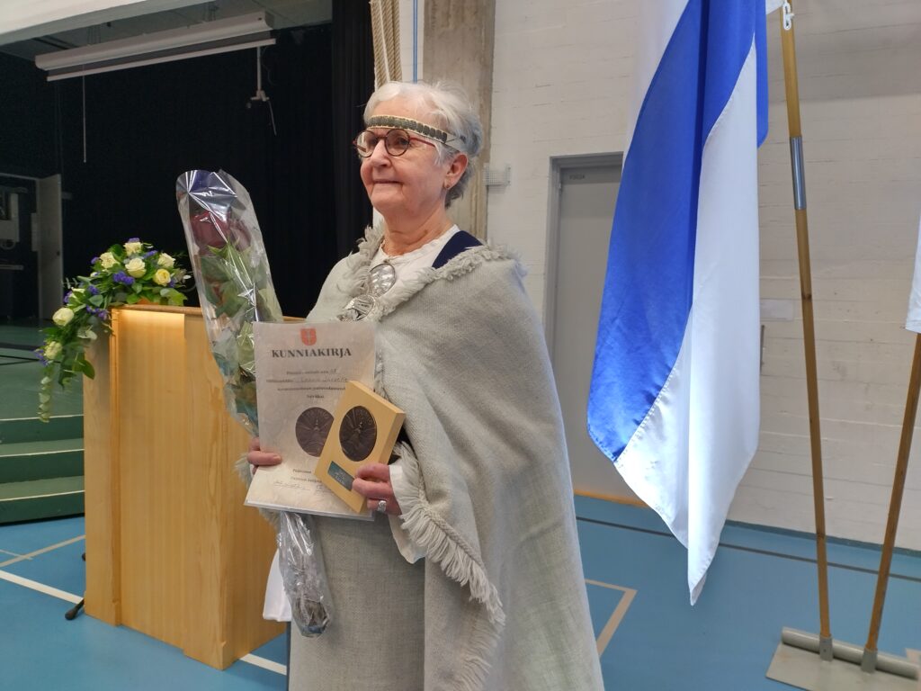 Leena Järvi Paimio-mitalin, kunniakirjan ja ruusun kanssa Vistan koulun juhlasalissa.