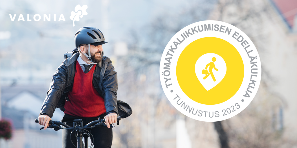 Iloinen henkilö pyöräilee kypärä päässä. Testissä lukee työmatkaliikkumisen edelläkulkija tunnustus 2023.