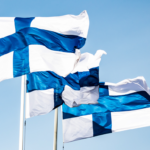Kolme Suomen lippua liehuu sinistä taivasta vasten.