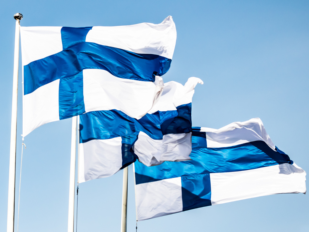 Kolme Suomen lippua liehuu sinistä taivasta vasten.