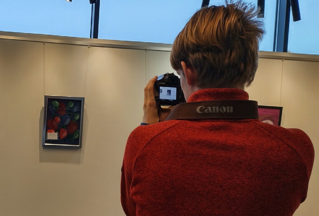 Nuorukainen kuvaamassa kameralla taidenäyttelyä.