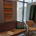 Erilaisia tekstiilitöitä näyttelyseinäkkeisiin ripustettuna että huonekalujen päällä.