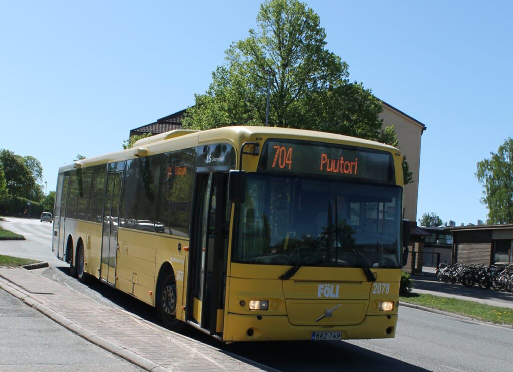 Keltainen Föli-bussi pysäkillä. Bussin inforuudussa lukee 704, Puutori.