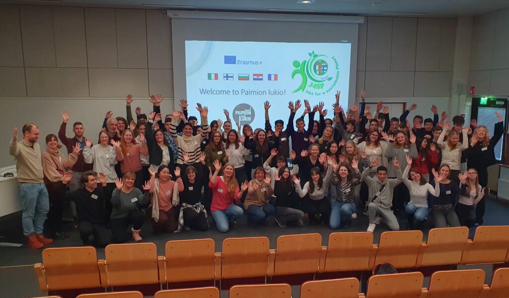 Ryhmäkuva kokoustilasta, jonka valkokankaalla lukee Welcome to Paimion lukio. Kuvassa näkyy myös eri maiden lippuja ja Erasmus-logo.
