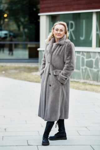 Vaaleatukkainen nainen seisoo talvitakissaan rakennuksen pihamaalla.