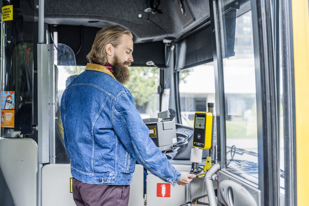 Mies maksamassaälypuhelimella bussimatkaa bussin etuosassa.