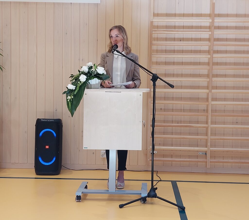 Vaaleatukkainen nainen puhumassa puhujakorokkeen ja mikrofonin takana.