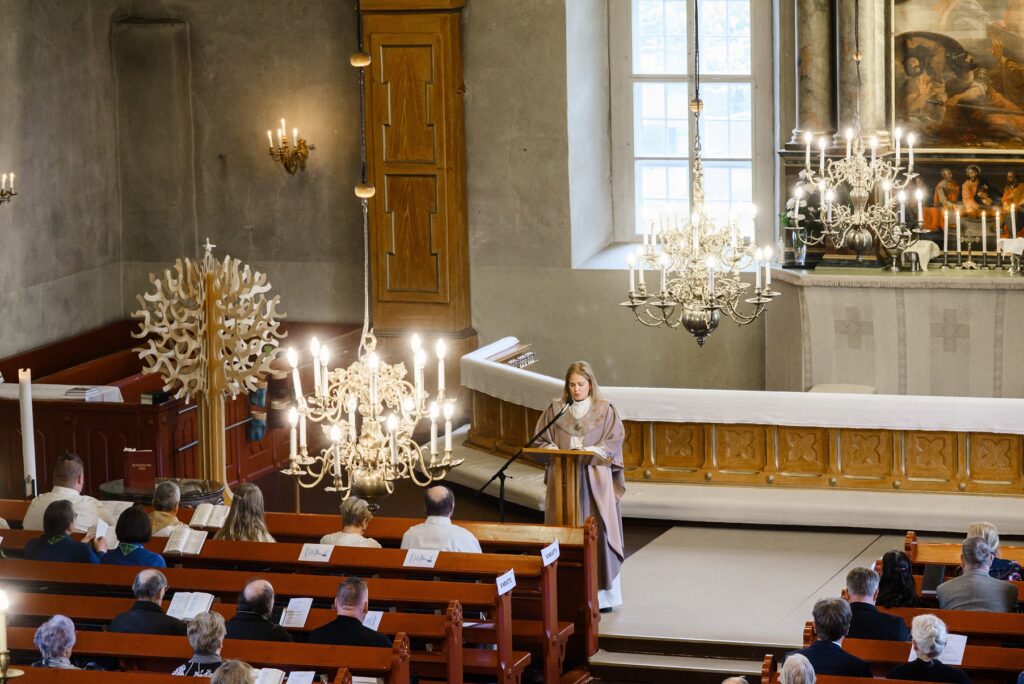Parvelta otettu kuva valaistusta kirkosta, jonka etuosassa piispa puhuu mikrofoniin. Penkeissä istumassa paljon ihmisiä.