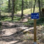 Helmi MTB Start kyltti ja metsäinen maisema, jossa menee maastopyöräily polku.