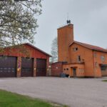 Kaksiosainen, ruskeasävyinen, rakennuskokonaisuus, jonka kyljessä teksti Paloasema. Rakennuksen edustalla asvalttikenttä.
