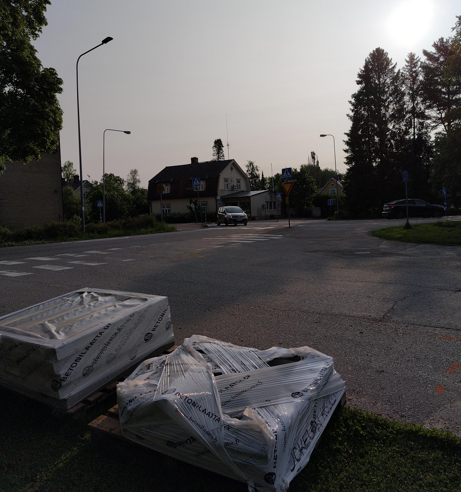 Katualueella otettu kuva, jossa tausta rakennuksia ja henkilöautoja, etualalla muovipäällystettyjä paketteja.
