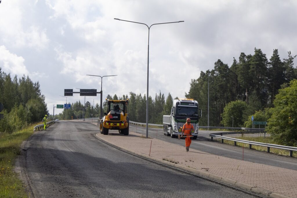 Tietyömaalla kaksi ajoneuvoa sekä yksi oranssiin asuun pukeutunut työntekijä.