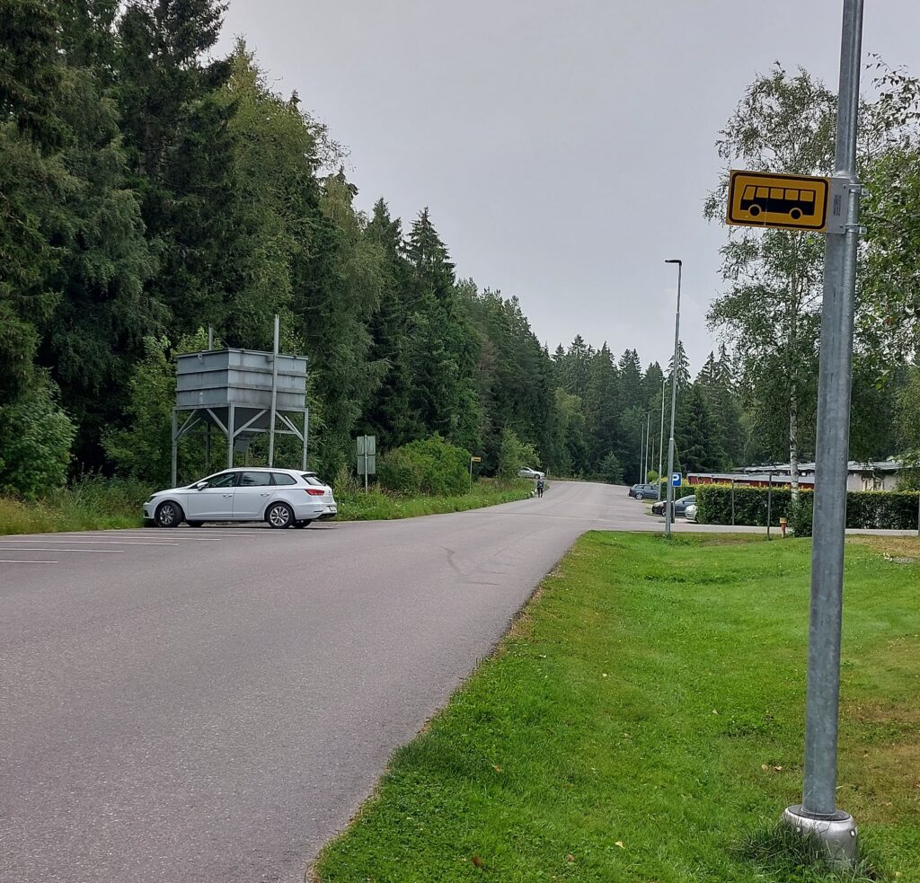 Asvalttitie, jonka varrella näkyy kaksi bussipysäkkiliikennemerkkiä.