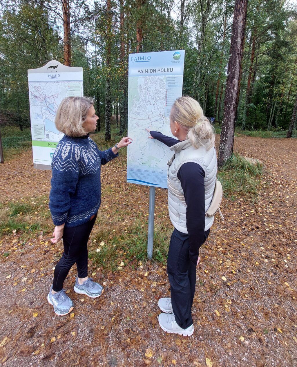 Kaksi naista seisoo reittitaulun edessä ja tutustuvat taululla esiteltävään reittiin.