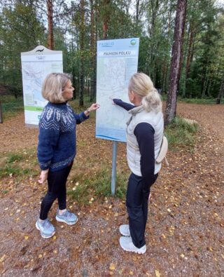 Kaksi naista seisoo reittitaulun edessä ja tutustuvat taululla esiteltävään reittiin.
