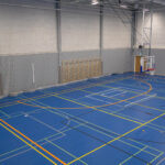 Sisäliikuntahallin vasenta osaa kuvattuna toisen kerroksen katsomosta. Seinällä puolapuut ja kuvassa myös pari koripallokoria ja voimistelurenkaat