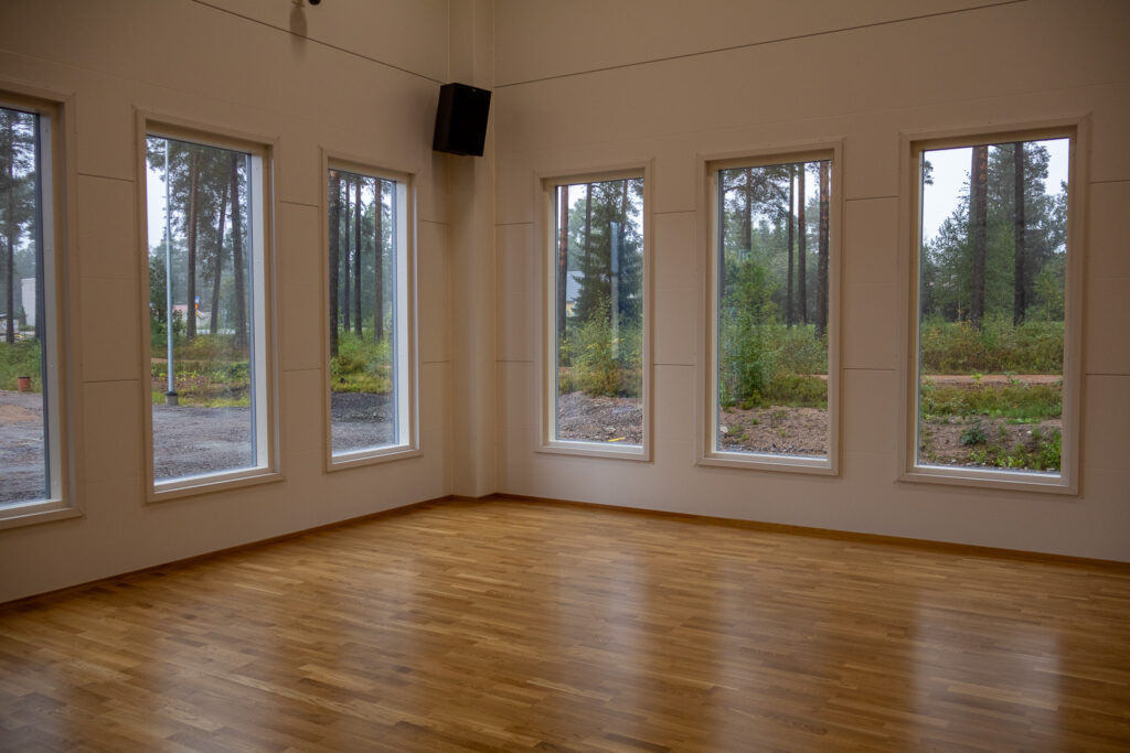 Sisäliikuntahallin monitoimisalit. Isoista ikkunoista näkyy parkkipaikka ja metsäinen maisema.