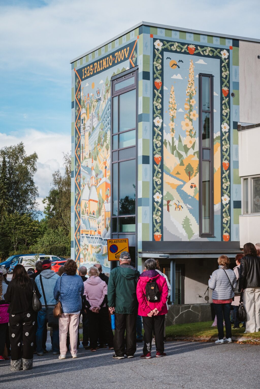 Runsaasti ihmisiä rakennuksen edustalla. Rakennuksessa kahdessa seinässä värikäs muraalimaalaus