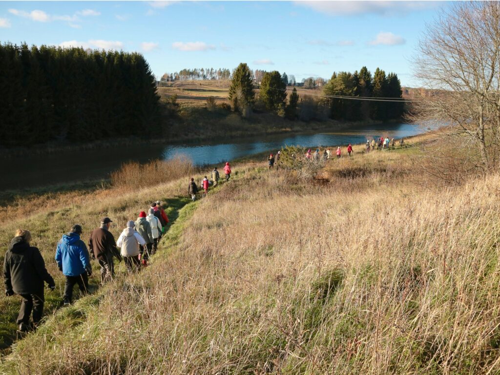 Runsaasti ihmisiä kävelemässä joen vartta myötäilevää polkua pitkin aurinkoisena syyspäivänä.