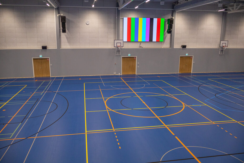 Sisäliikuntahallin liikuntasalia kuvattu toisen kerroksen katsomosta keskeltä. Keskellä seinällä on iso näyttötaulu.