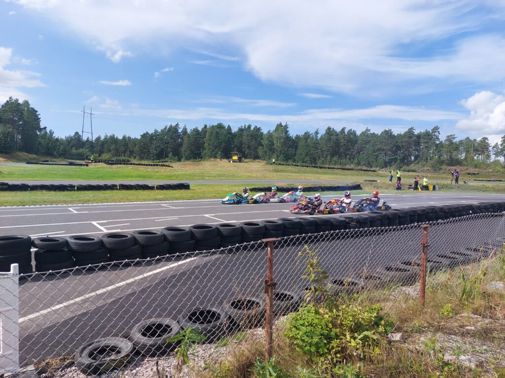 Useita karting-autoja ajamassa radalla. Etualalla renkaita suojavallina.