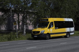 Pääosin keltainen pikkubussi, jonka tuulilasin yläosassa teksti P5 Palvelulinja. Auto on pysäkillä asvallttitiellä.