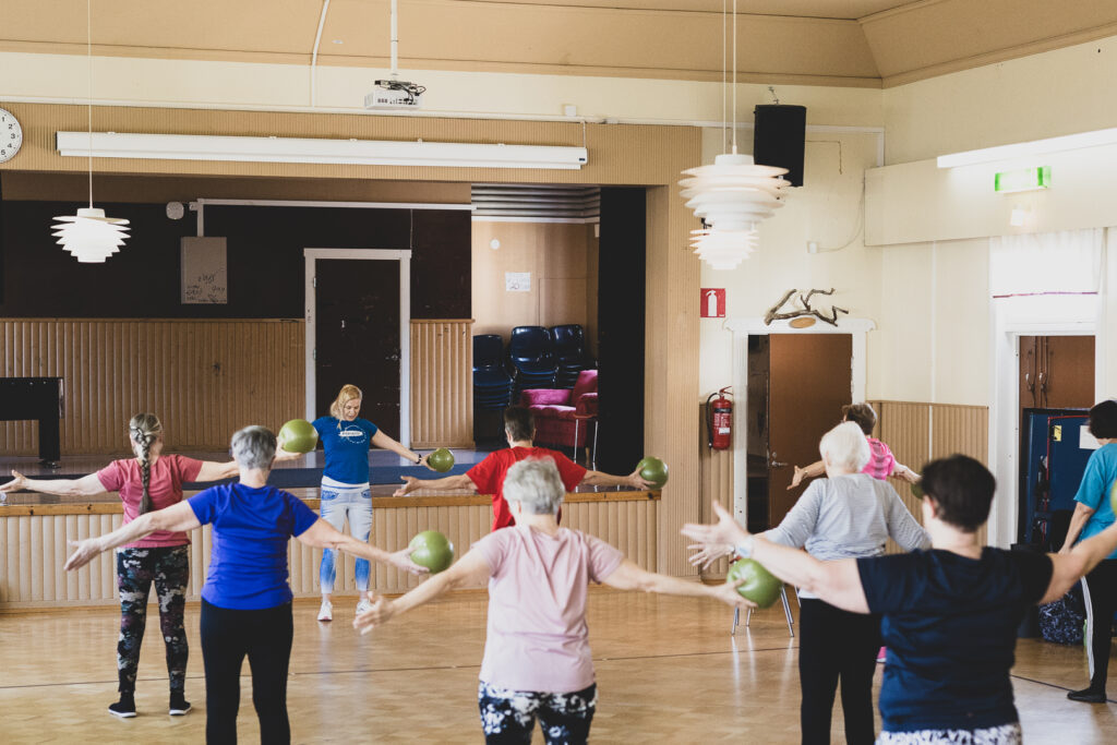 Kurssilaisia salissa kädet ylhäällä jumppatunnilla