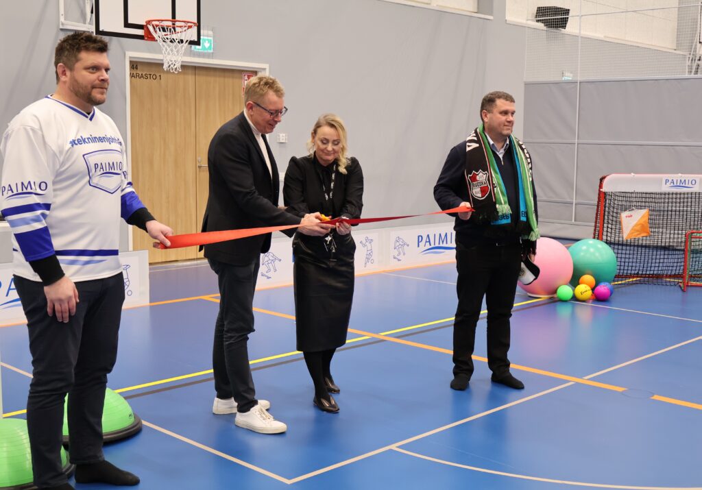 Kaksi miestä pitää punaista nauhaa kireänä ja yksi mies ja yksi nainen leikkaavat saksilla nauhan poikki.