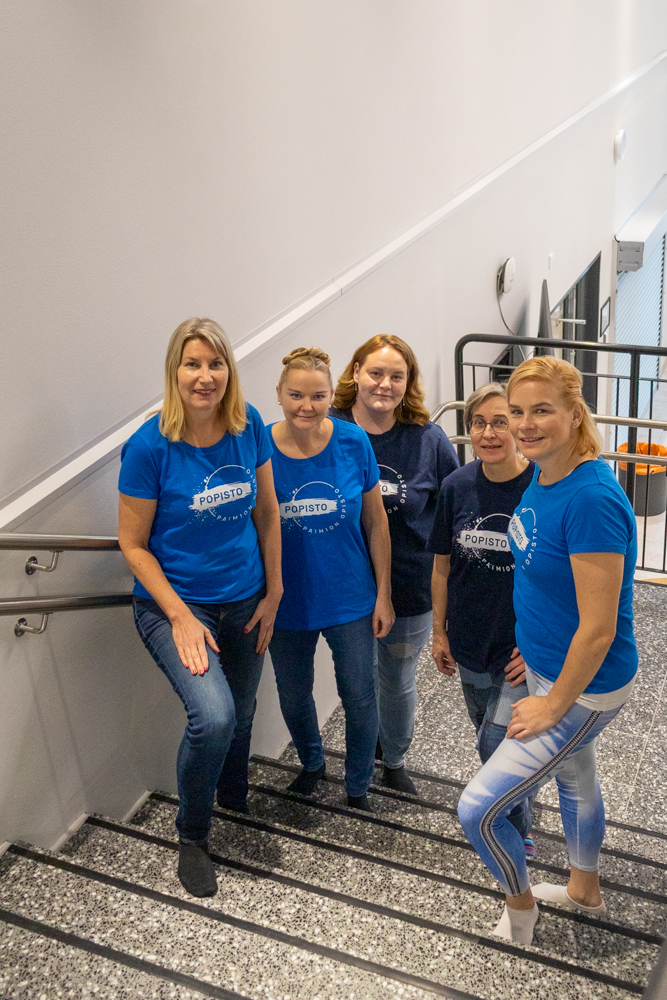 Viisi naista portaikossa päällään siniset t-paidat