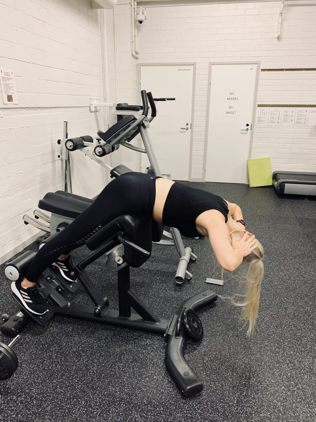 Kuntosalilaite, jossa kuntoilemassa vaaleatukkainen nainen.