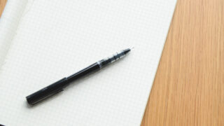 Pöydällä tyhjä vihko ja kynä paperin päällä.