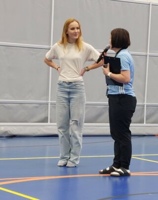 Tummatukkainen nainen haastattelee vaaletaukkaista naista sisäliikuntahallin lattialla.