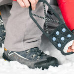 Kuvassa talvijalkine lumessa ja henkilöllä kädessä liukuesteet, jotka voi laittaa kenkiin.