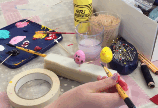 Lapsen käsi pielee sivellintä pääsiäisaskartelun päällä