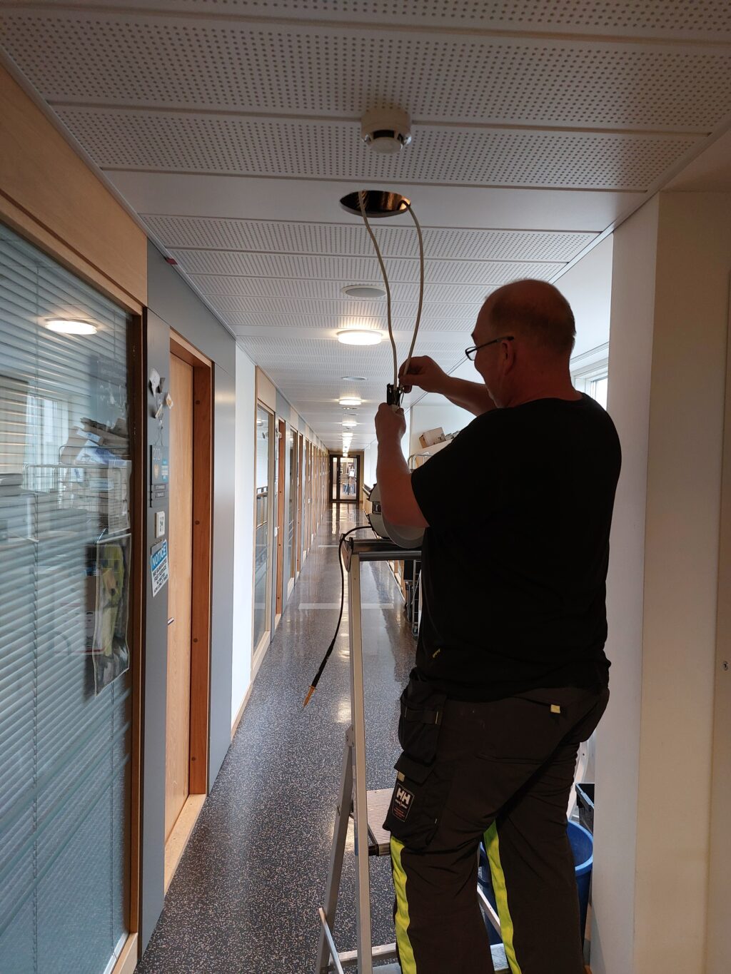 Sähköasentaja vaihtamassa käytävän katon valaisinta.