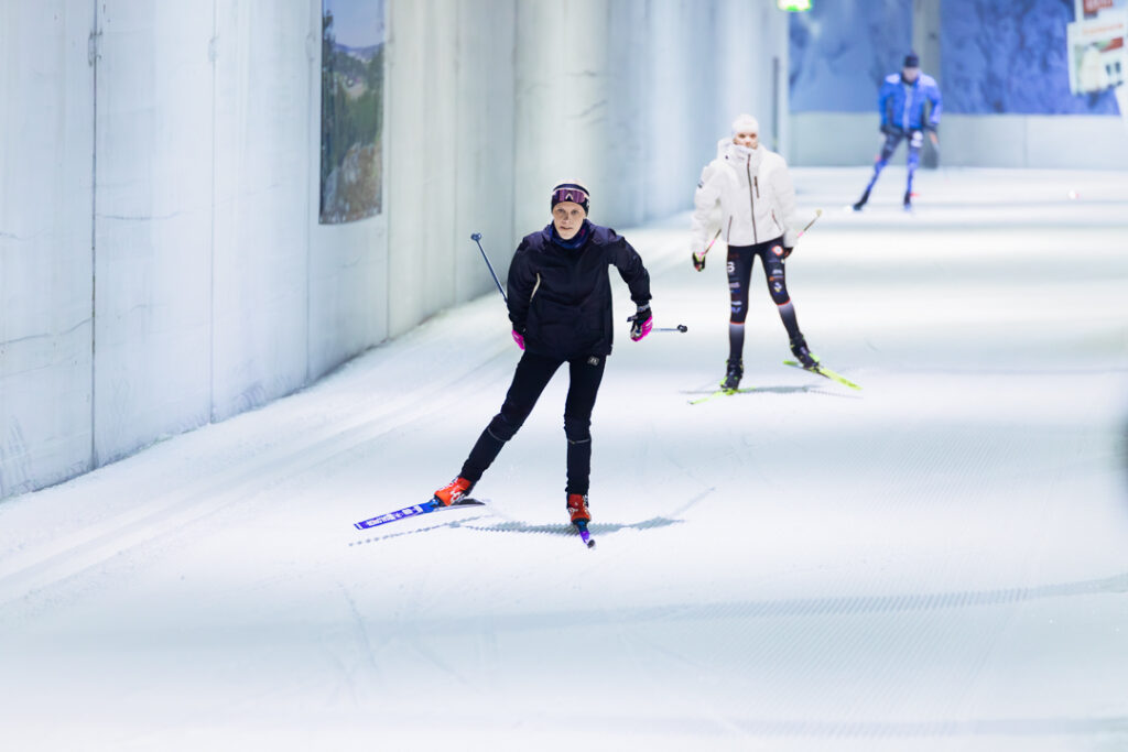 Kolme henkilöä hiihtää kohti kameraa hiihtotunnelissa.