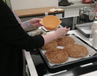 Leivinpellillä neljää leipää, joita henkilö on juuri voitelemassa.