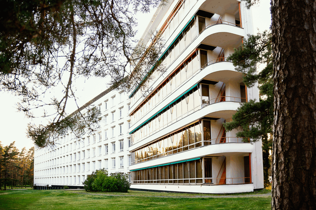 Suuri valkoinen rakennus kuvattuna metsän suunnasta.