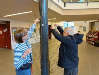 hyte-koordinaattori Matleena sekä Juhani ripustamassa heijastimia puuhun kaupungintalon aulassa